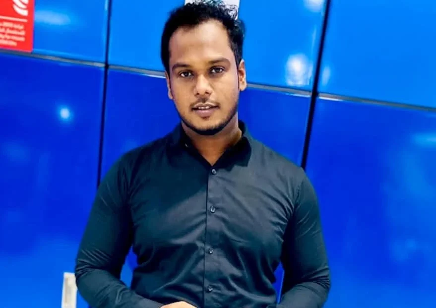 A man in a blue shirt and light grey pants stands holding a phone, against a blue background, representing a top freelance digital marketer in Thrissur.