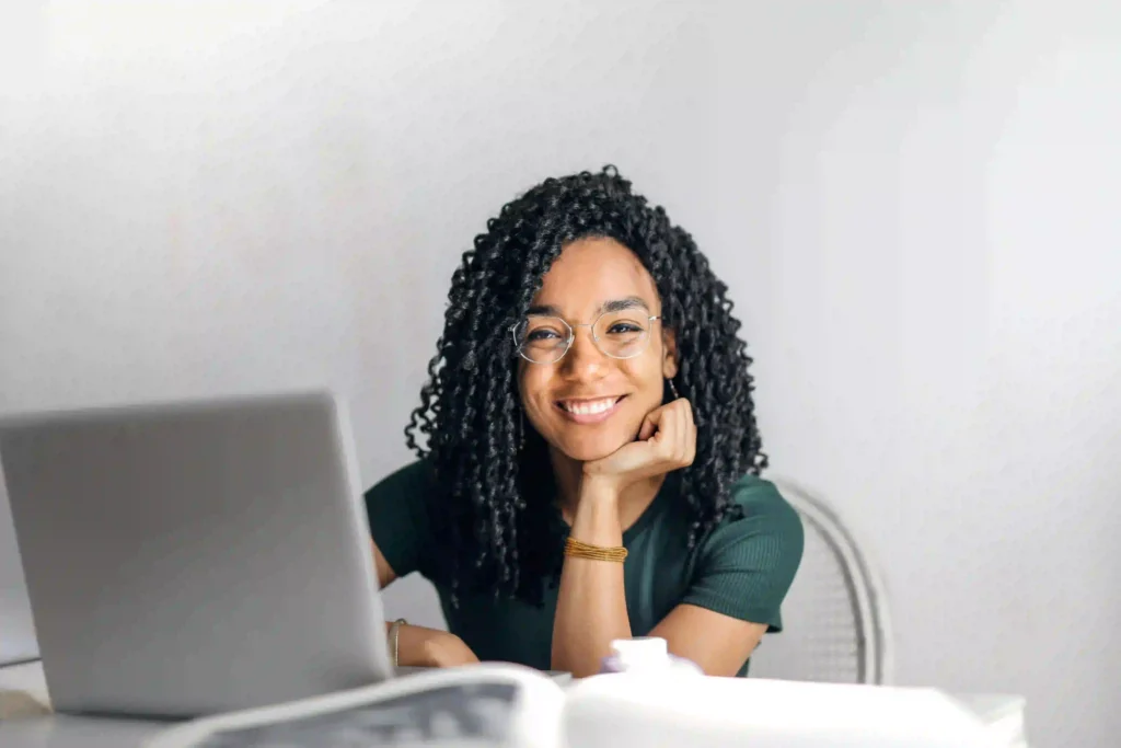 A woman with curly hair and glasses rests her chin on her hand while sitting at a desk with a laptop, representing a freelance digital marketer in Thrissur.